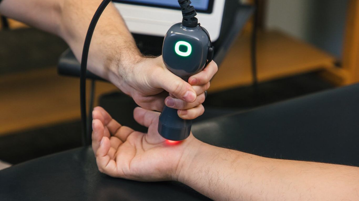 A person uses a device to treat another person's wrist with red light.