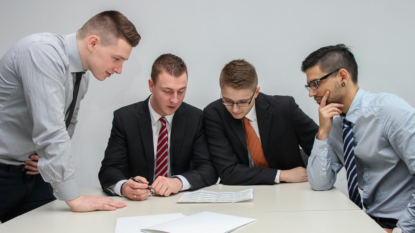 four men looking to the paper on table