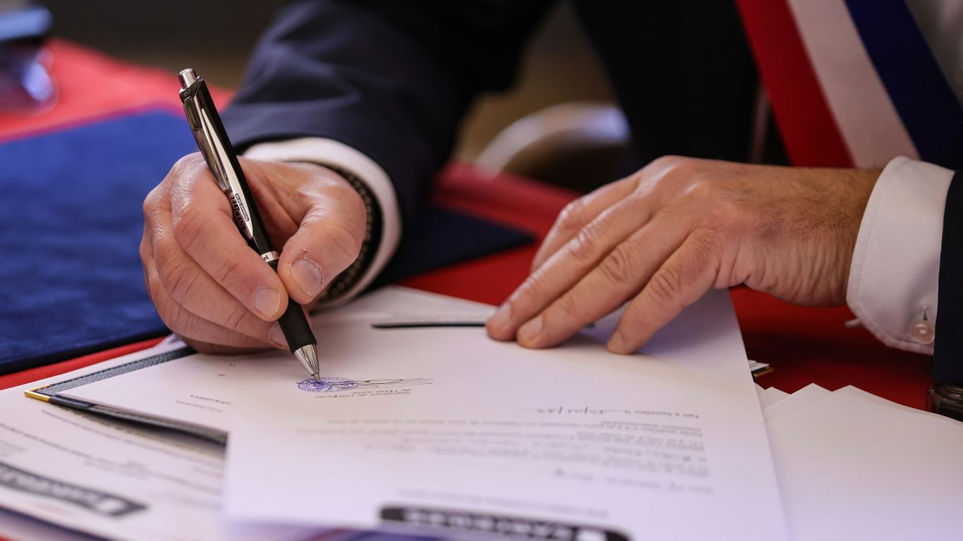 A person signs a document with a pen.