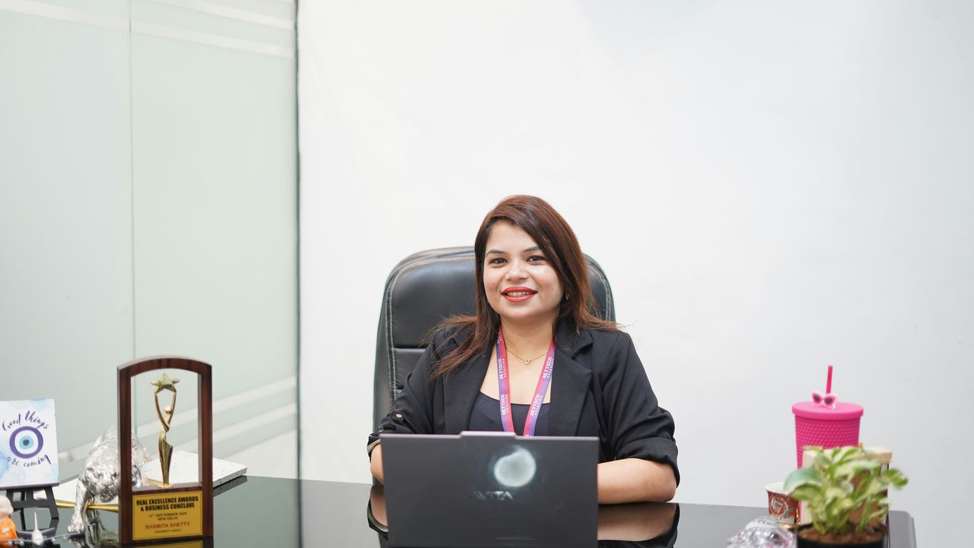 A smiling woman sits at a desk with a laptop.
