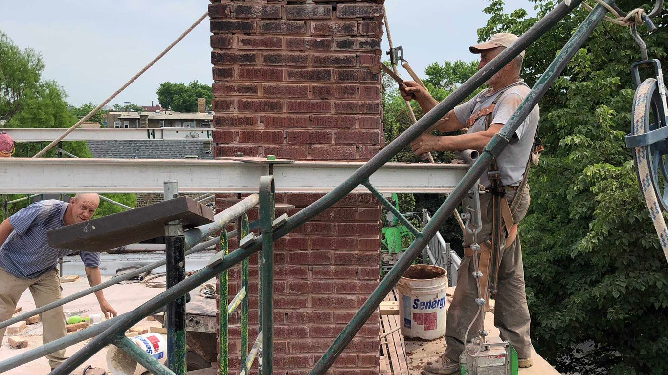Workers on scaffolding repairing a brick chimney on a cloudy day.
