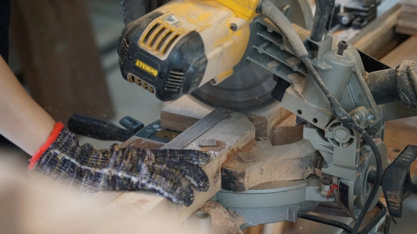 A person wearing a glove cuts wood with a miter saw.