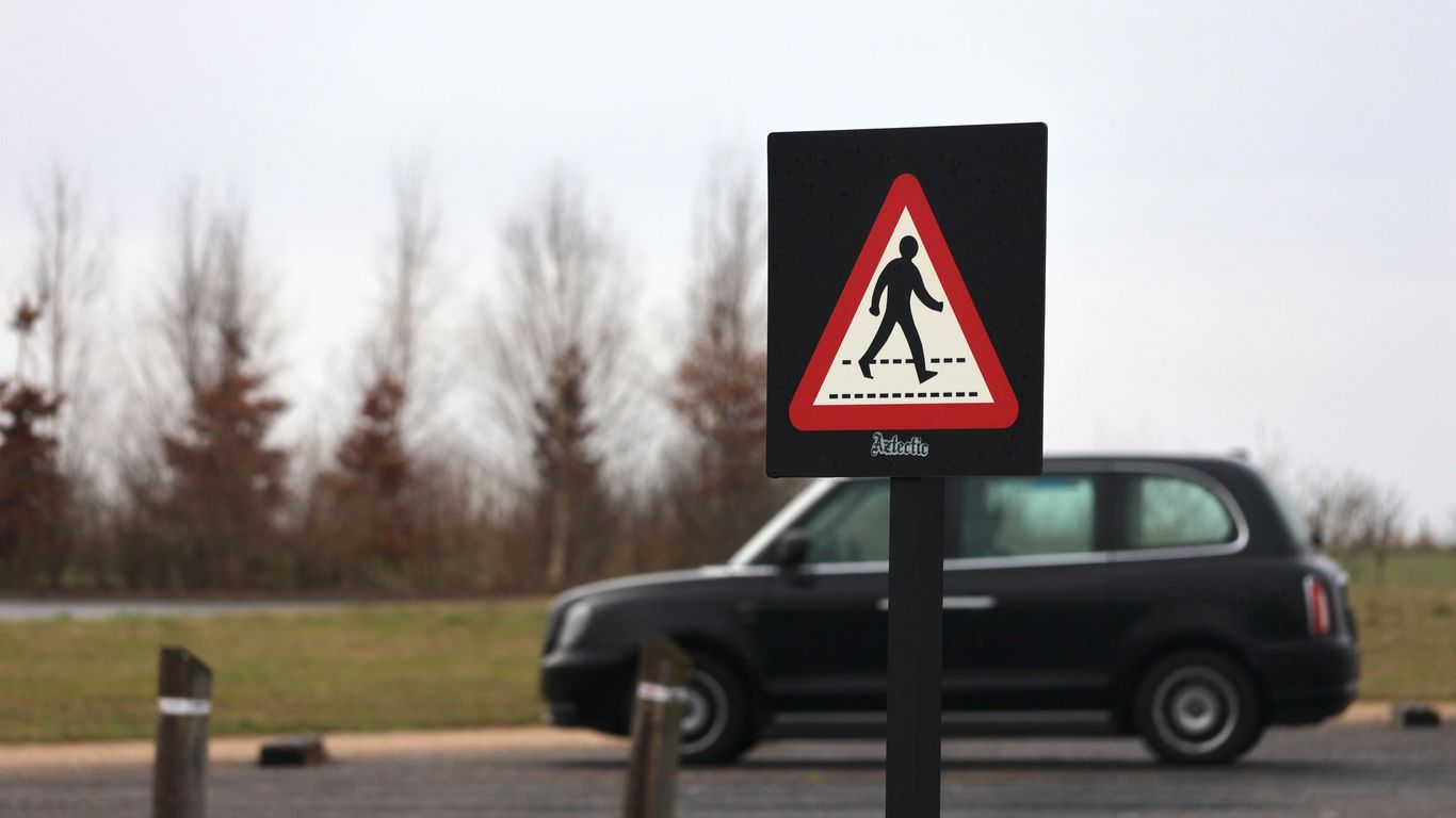 A car driving down a road next to a pedestrian crossing sign