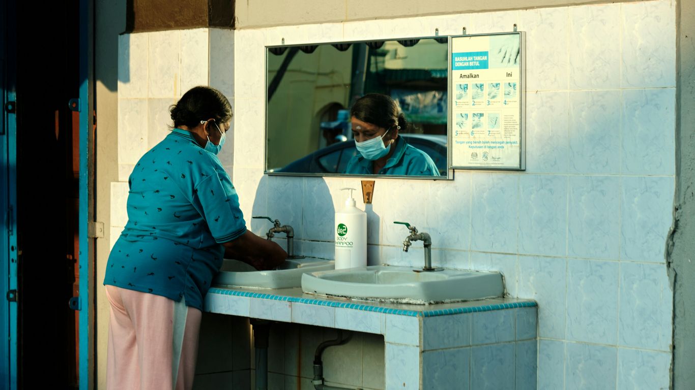 a woman wearing a face mask washes her hands in a sink