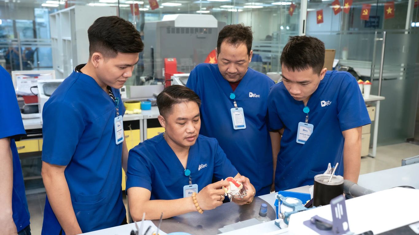People in blue scrubs examine a dental model in a laboratory setting.