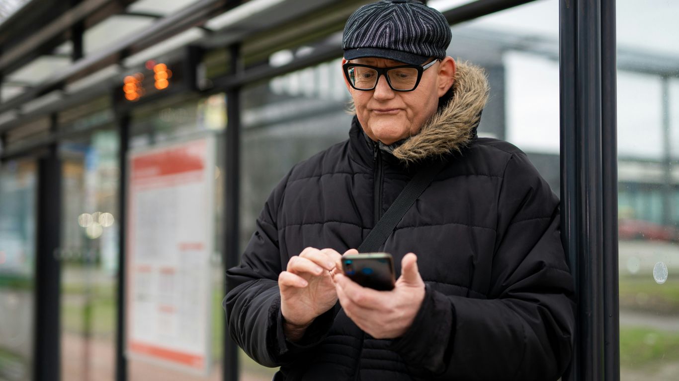 a man in a black jacket and a black hat looking at his cell phone