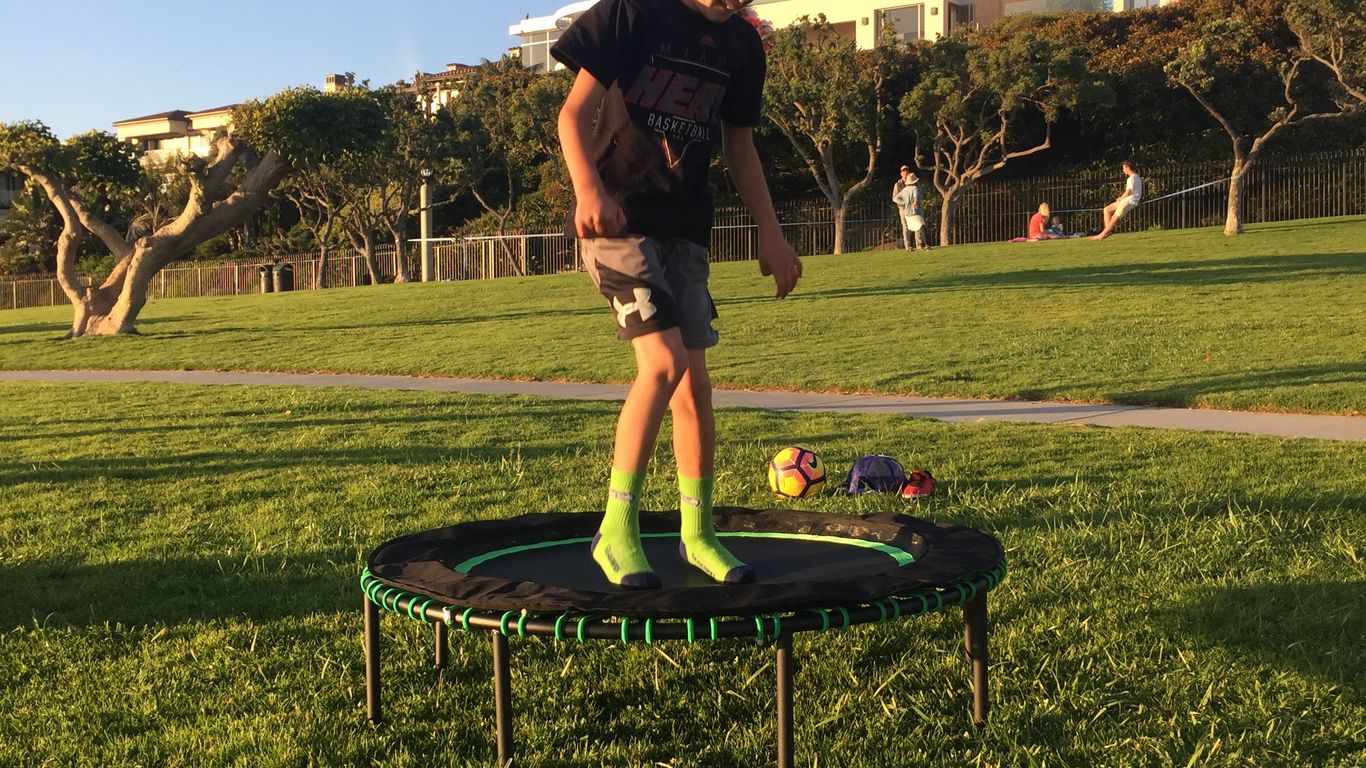 Person standing on trampoline in park, houses in background.