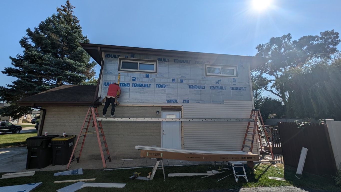 House siding being installed on a sunny day with ladders and materials.