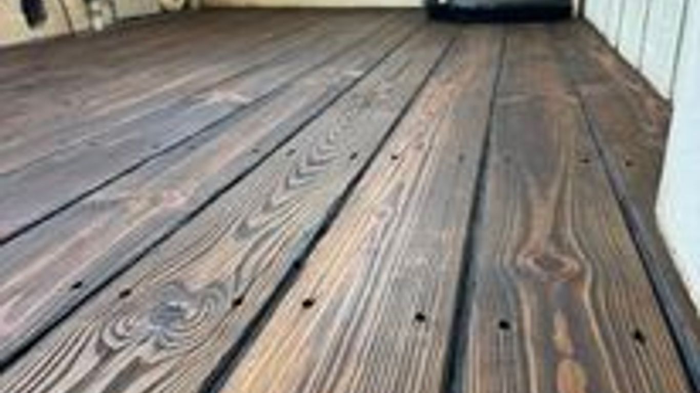 Wooden floorboards with a dark finish and appliances in background.