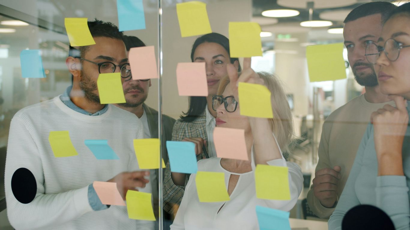 Team brainstorms using sticky notes on glass wall