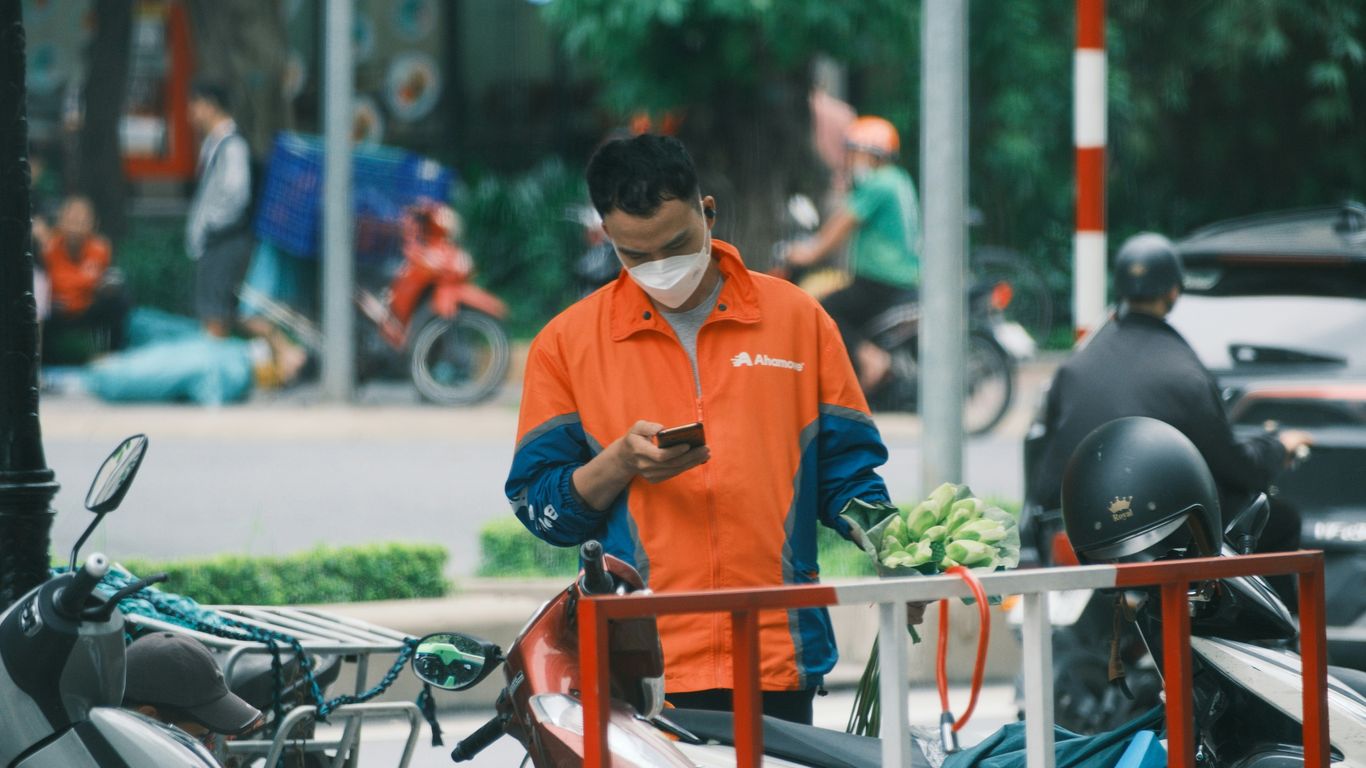A delivery person looks at his phone outdoors.