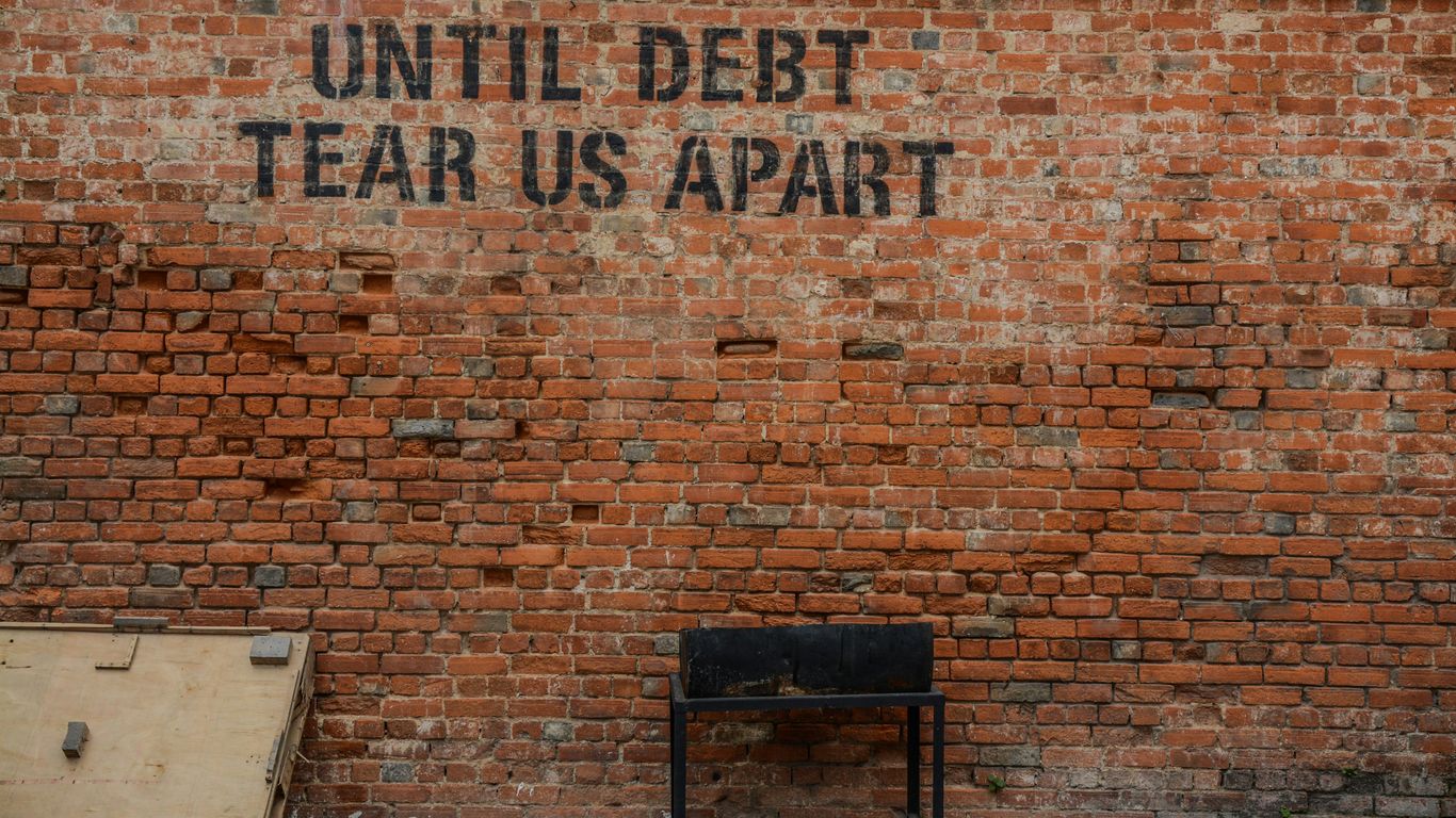 Until debt tear us apart printed red brick wall at daytime