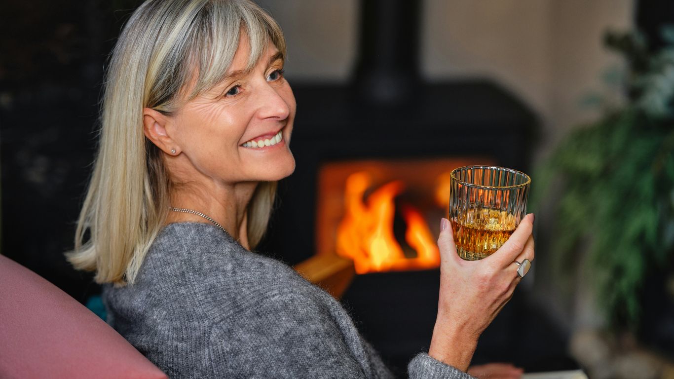 a woman holding a glass of wine in front of a fireplace