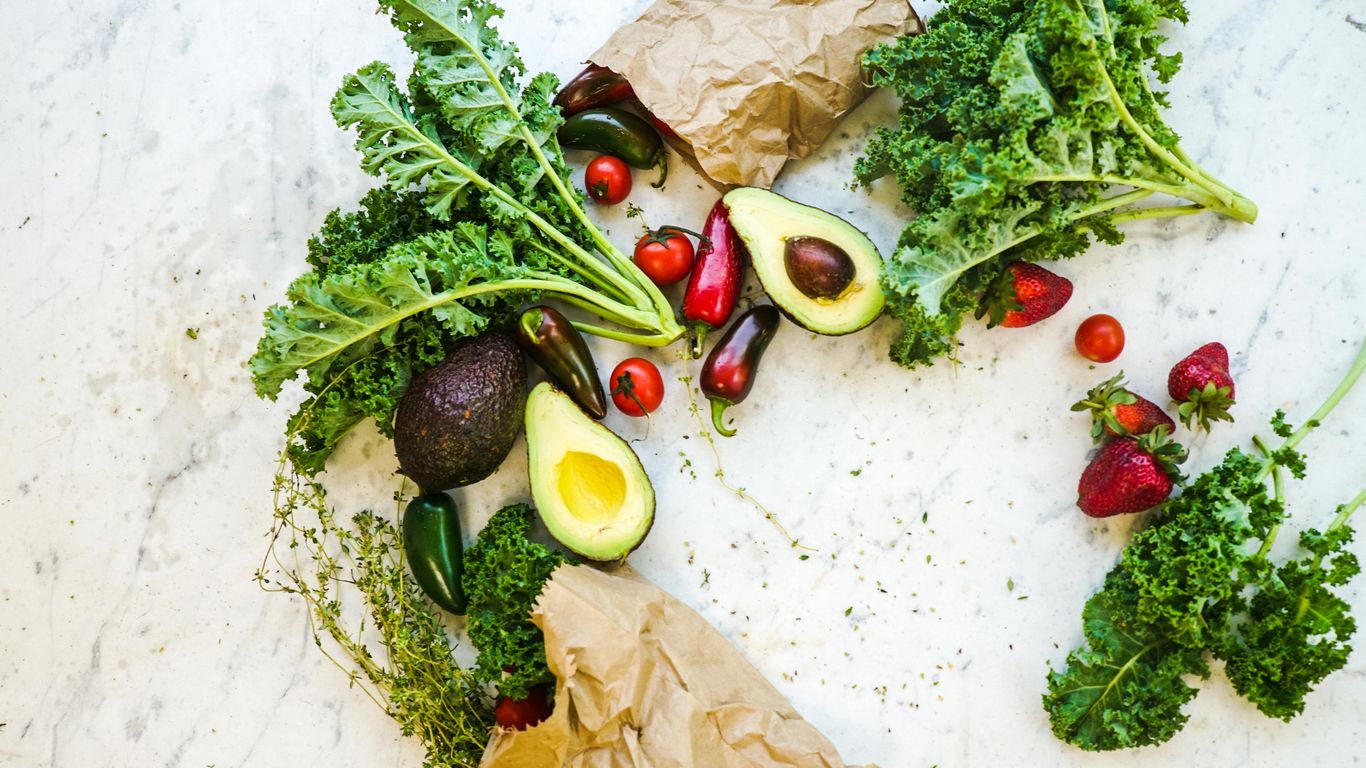 Fresh vegetables and fruits, including kale, avocado, strawberries, tomatoes.