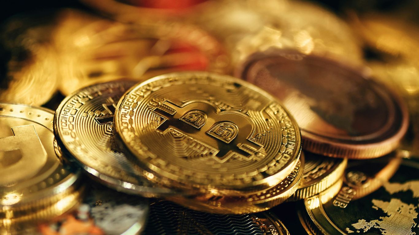 A collection of shiny, gold-colored cryptocurrency coins scattered.