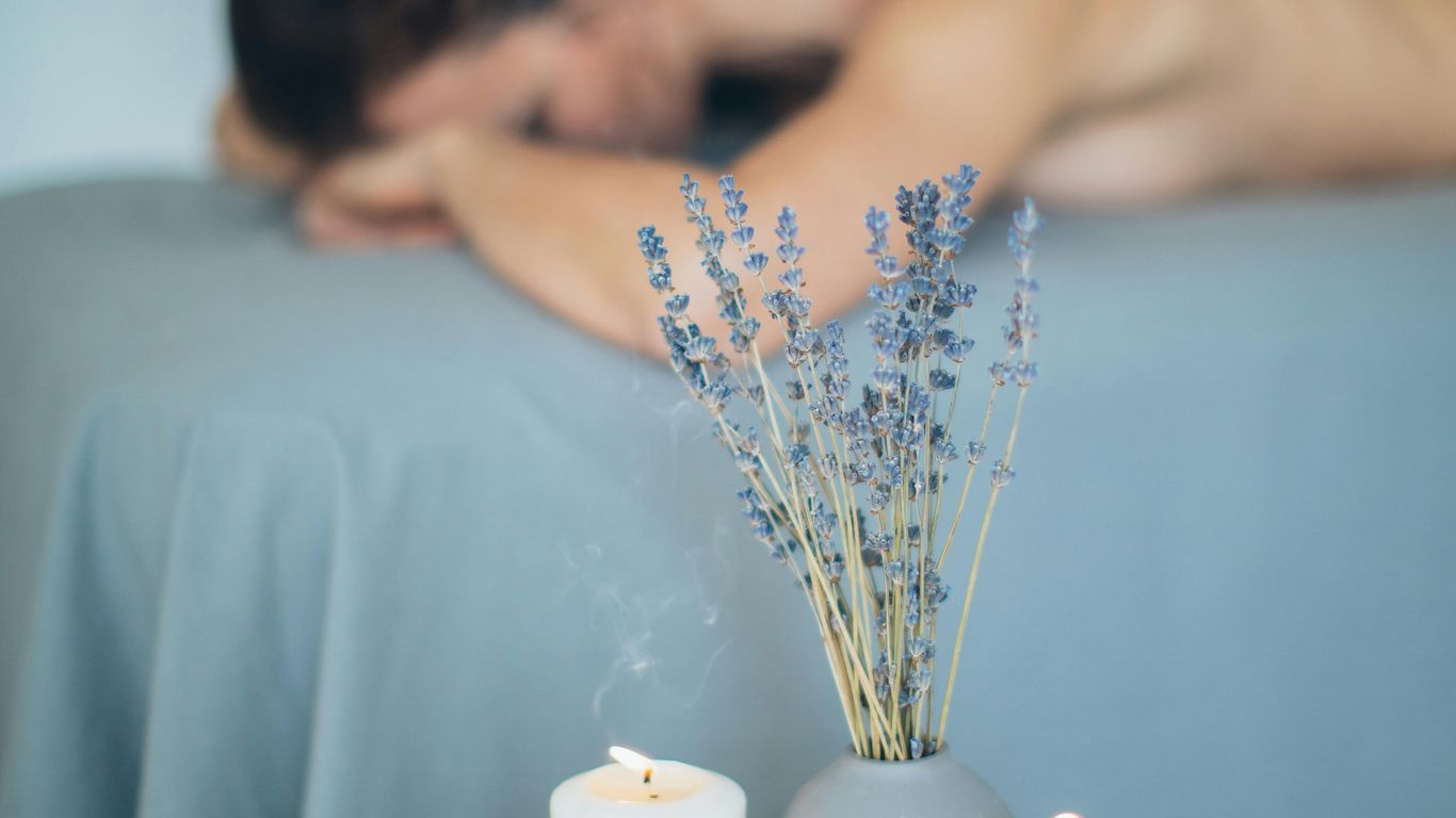 Person receiving massage, candles and lavender create relaxing atmosphere.