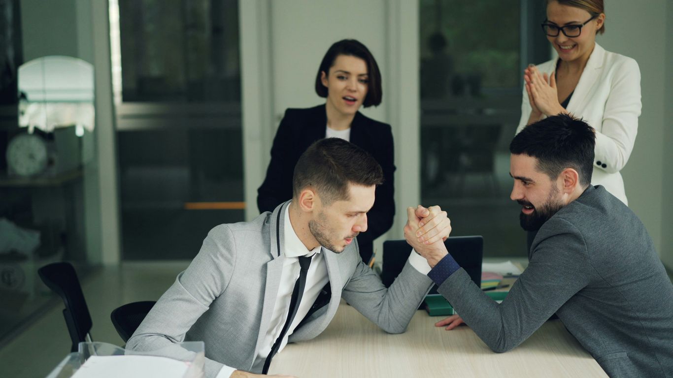 Two businessmen arm wrestling while colleagues watch