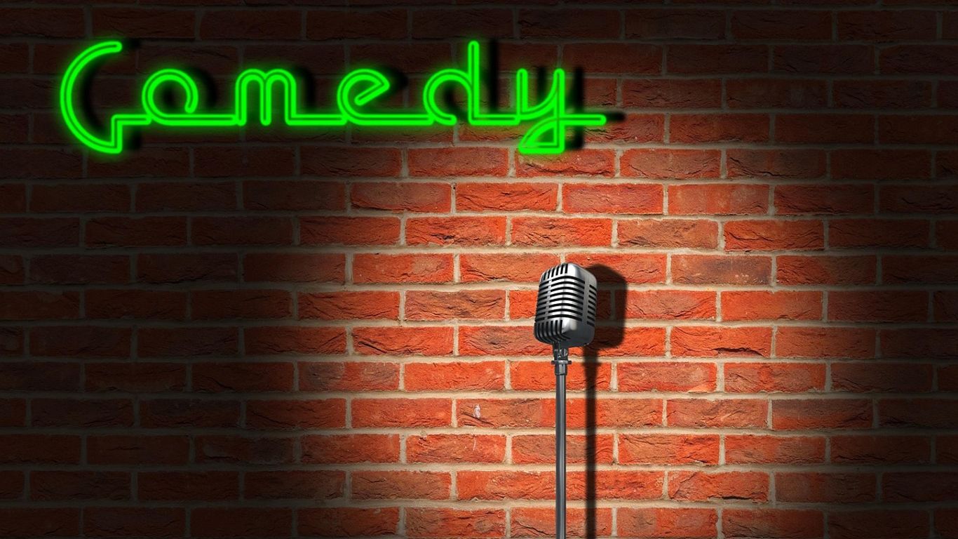 A microphone stands in front of a brick wall, "Comedy" sign.
