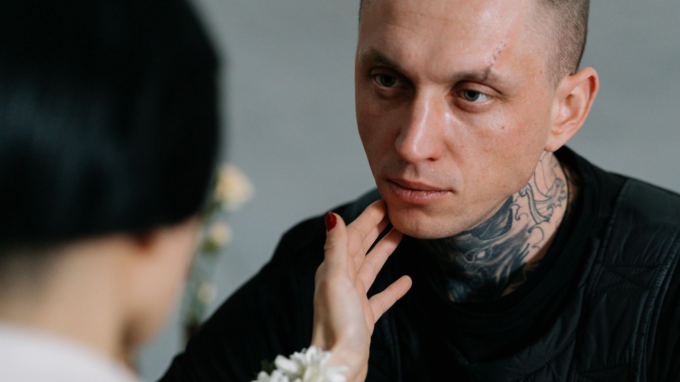 Person with tattoos being gently touched on the face, emotional moment.
