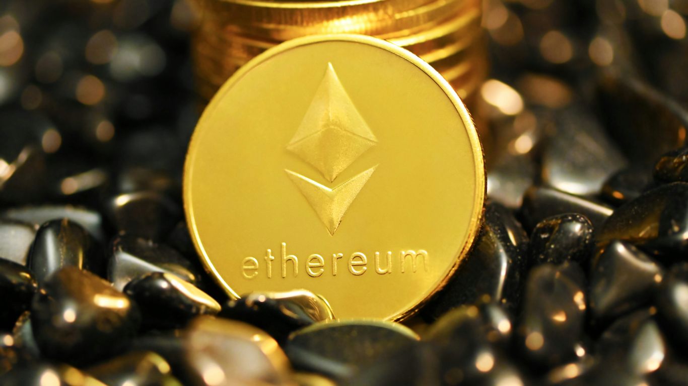 A gold Ethereum coin resting on shiny black stones.