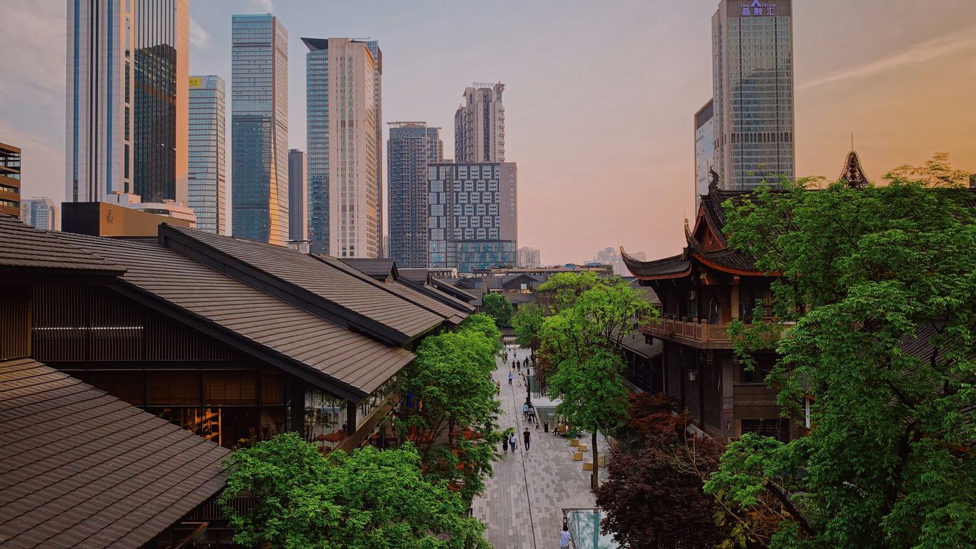 Modern skyscrapers overlook traditional buildings and trees.