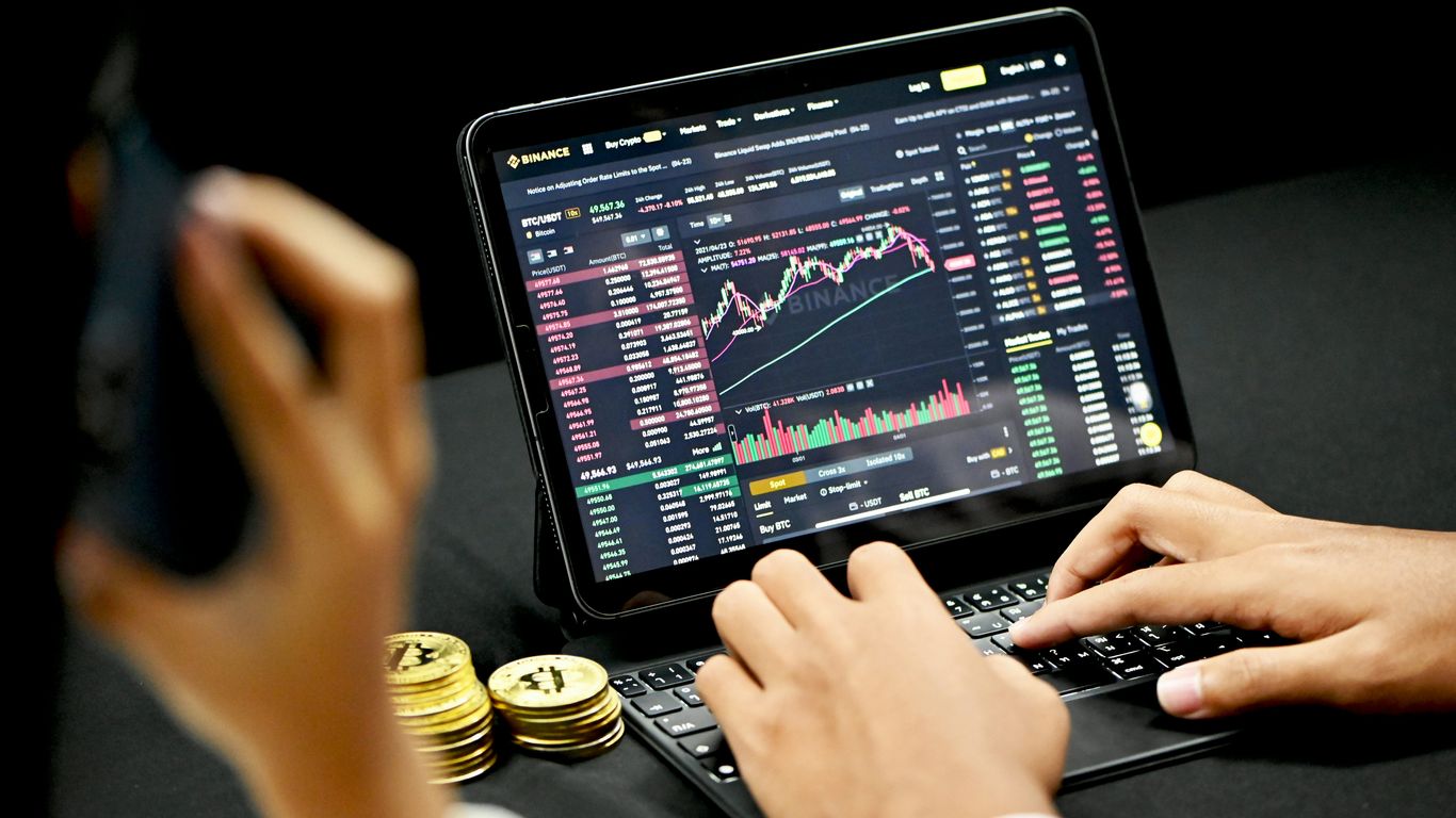 Person using a tablet for cryptocurrency trading with coins nearby.