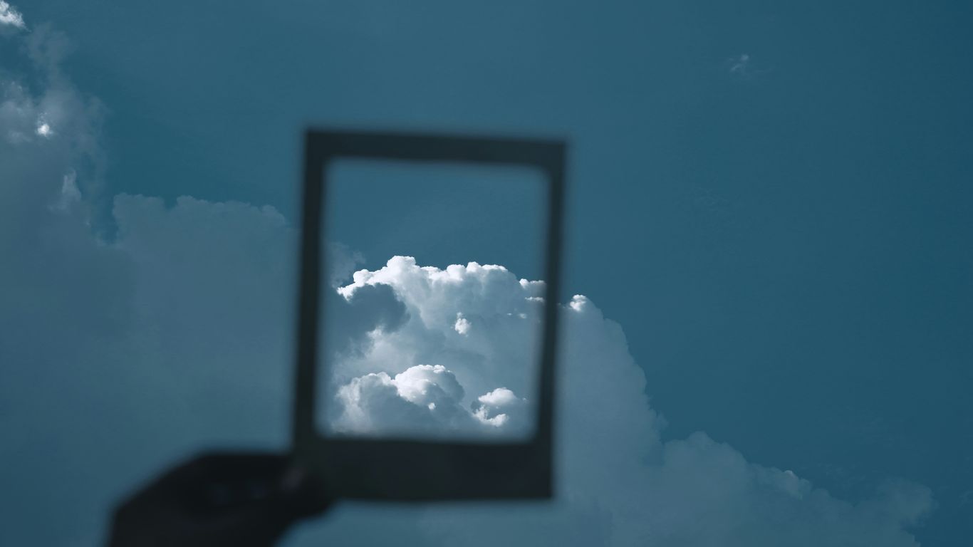 a hand holding up a square mirror in the sky