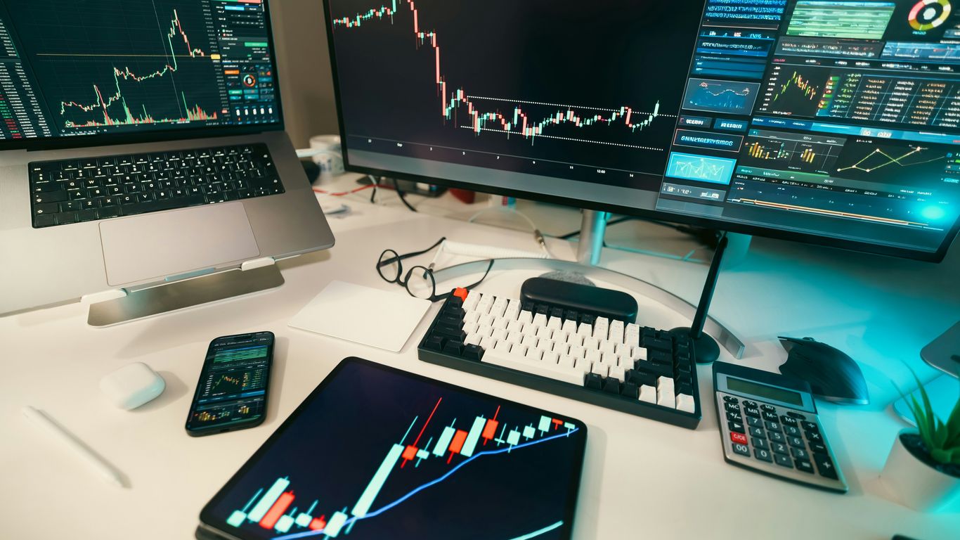 Stock charts are displayed on multiple screens.
