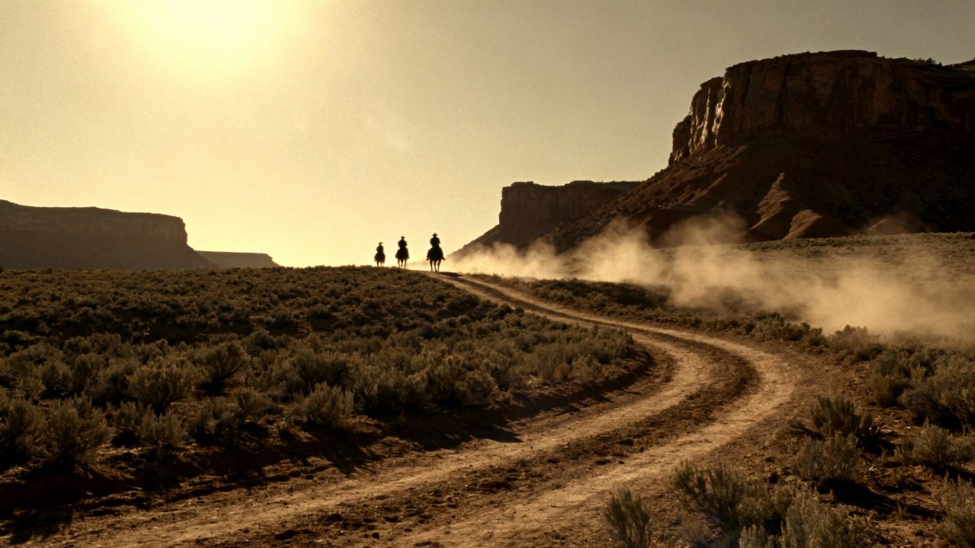 Cowboys riding horses in a dusty Western landscape.