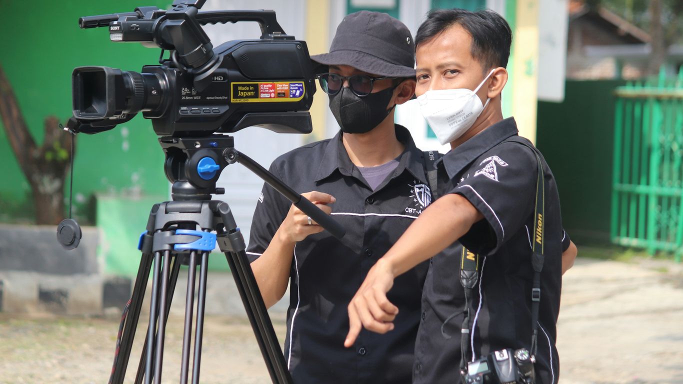 man in black polo shirt wearing white mask holding black camera