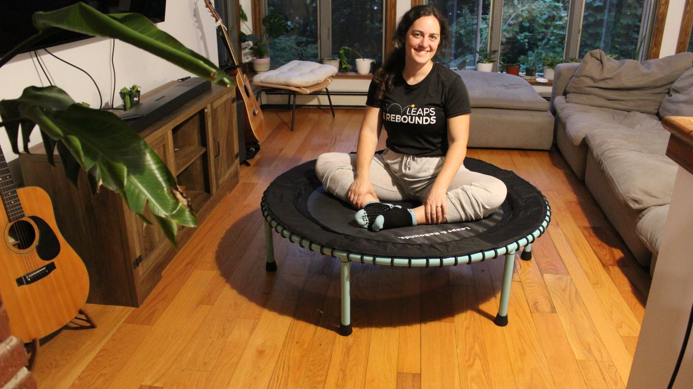 Person sitting cross-legged on mini trampoline in cozy living room.