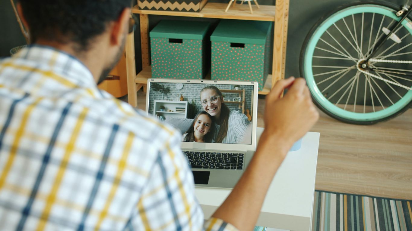 Man video calling two smiling women on laptop.