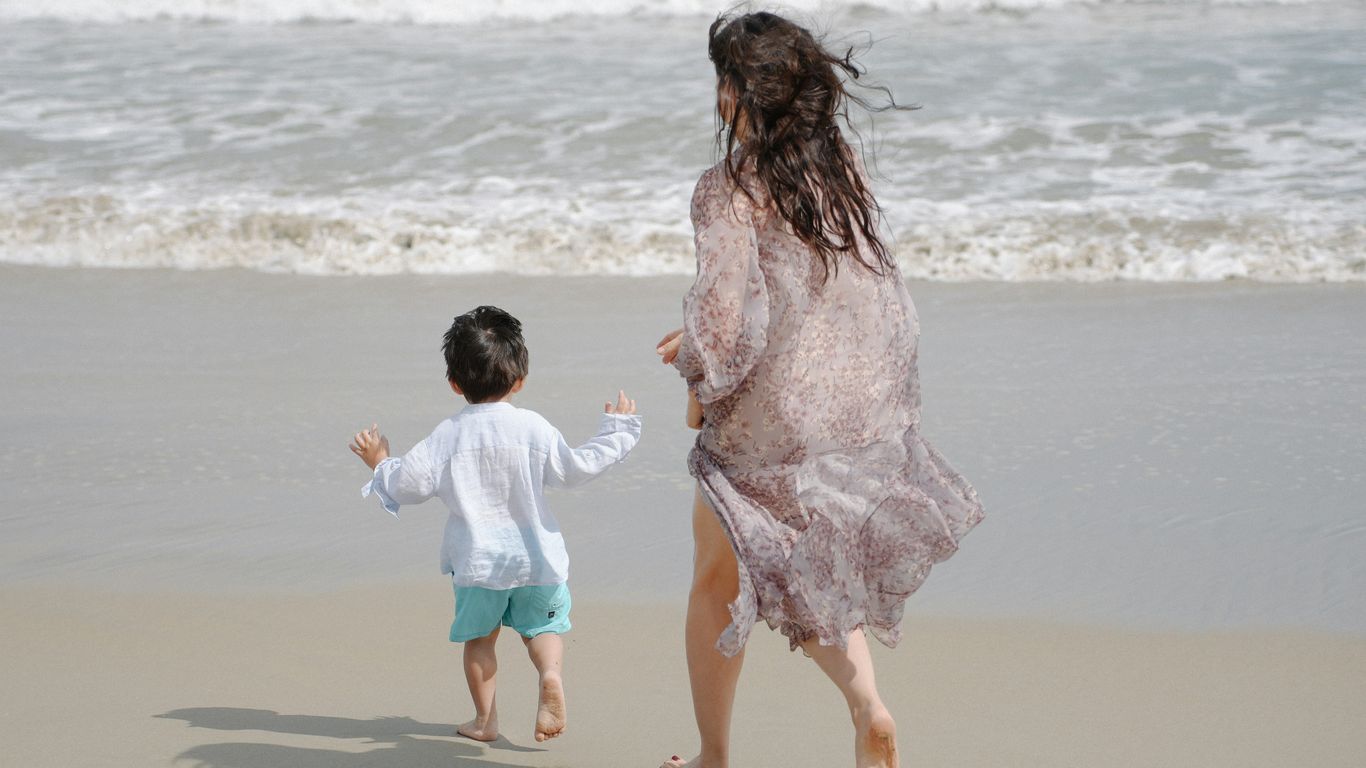 Mother and child running on a sandy beach.