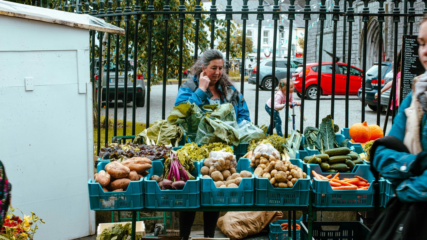 a woman talking on a cell phone next to a table full of vegetables