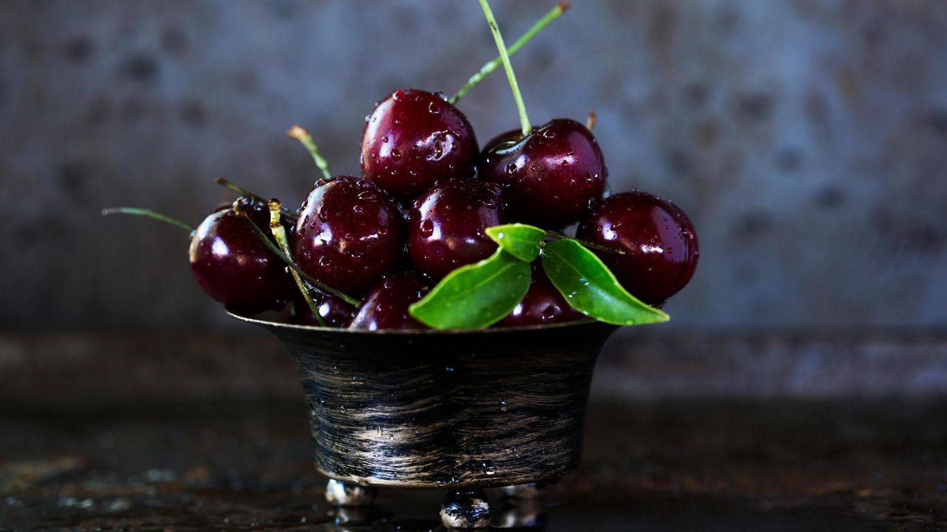 A bowl of fresh cherries with green leaves, water droplets.
