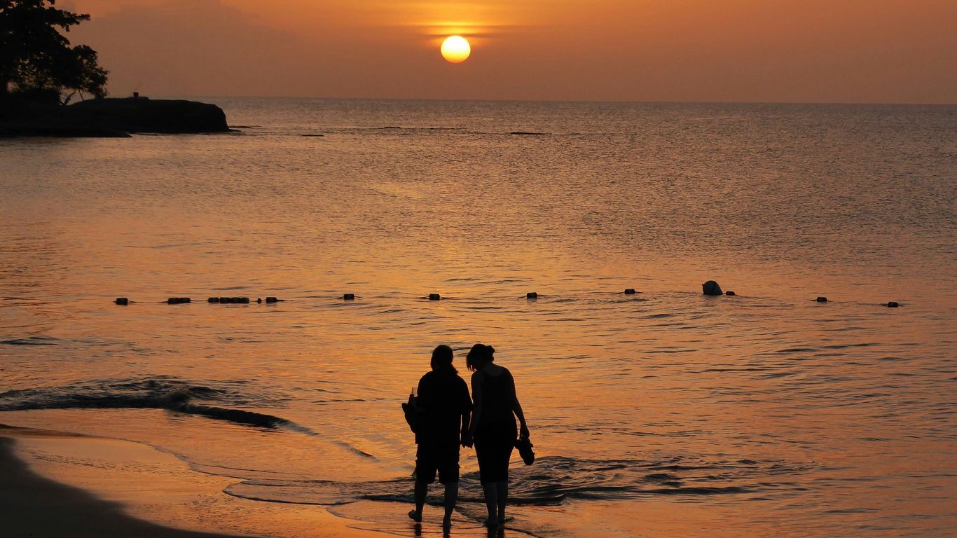 silhouette of 2 people standing on beach during sunset