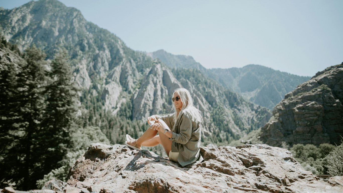 woman sitting on rocky hill viewing mountain under blue skies