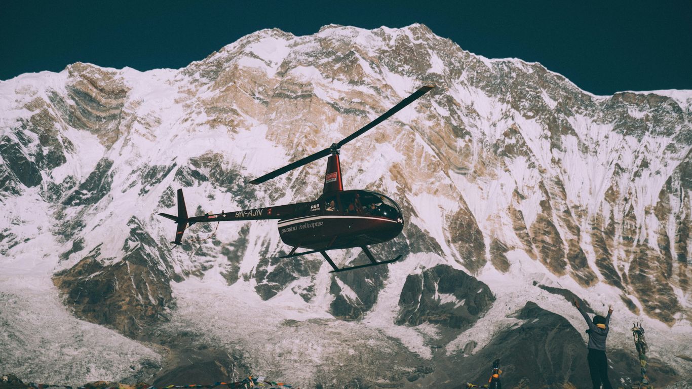 black and red helicopter flying over snow covered mountain during daytime