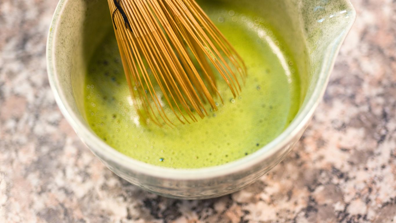 Matcha tea being whisked in a bowl.