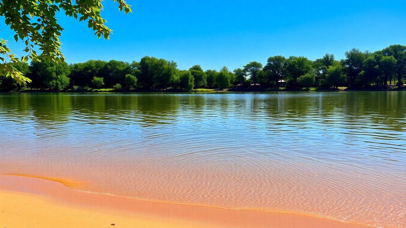 Calm lake reflecting blue sky with green trees.