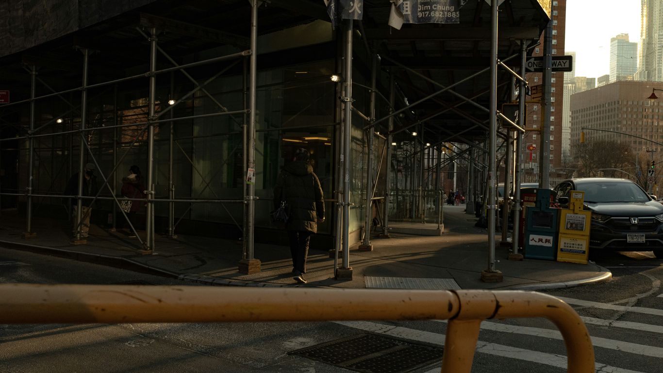a man is walking across the street in front of a building with scaffolding