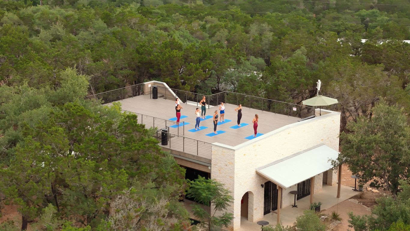 People practice yoga on a rooftop deck surrounded by trees.