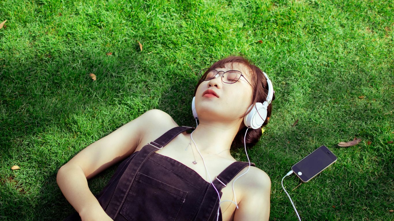 a woman laying on the grass listening to music