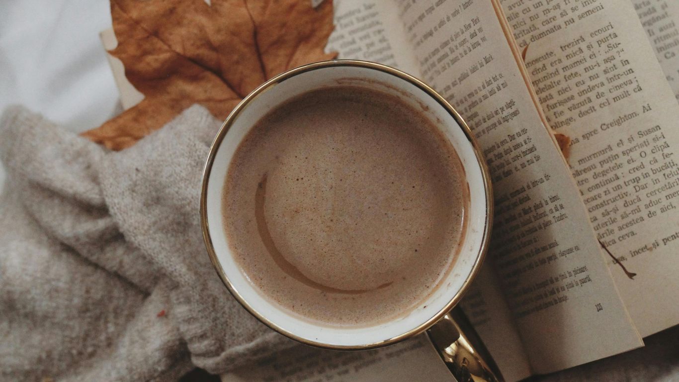 Cup of coffee, open book, sweater, and autumn leaves.