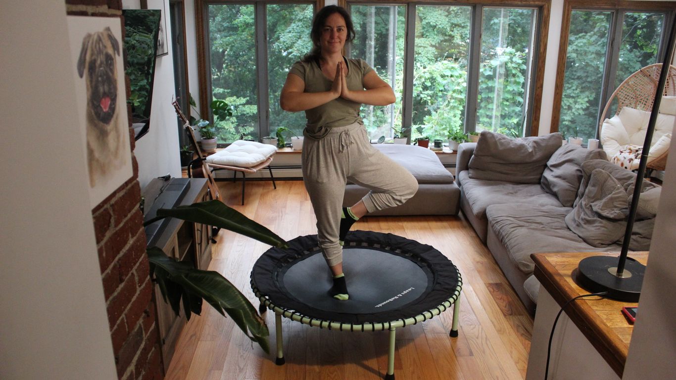 Person balancing on trampoline in living room, surrounded by plants.