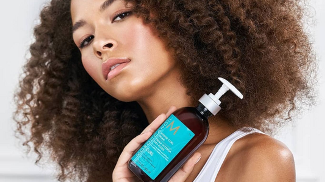 Person holding hair product bottle, showcasing healthy curly hair.