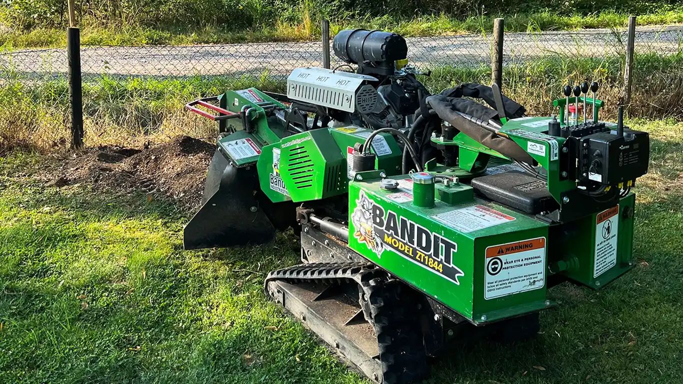 A green Bandit tree stump grinder on grassy terrain.