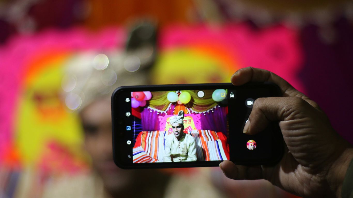 person taking photo of man in traditional shirt with smartphone