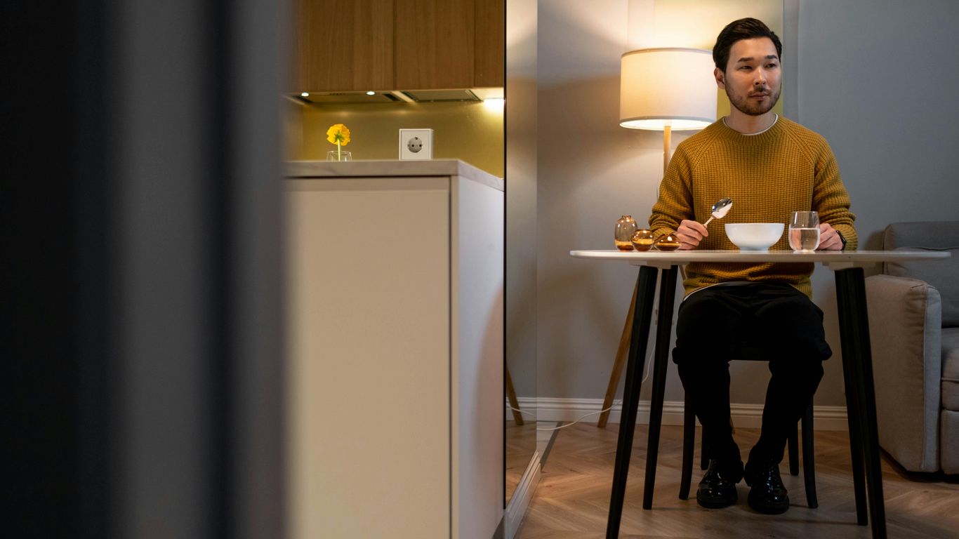 Person sitting at table with food, lamp, and kitchen background.