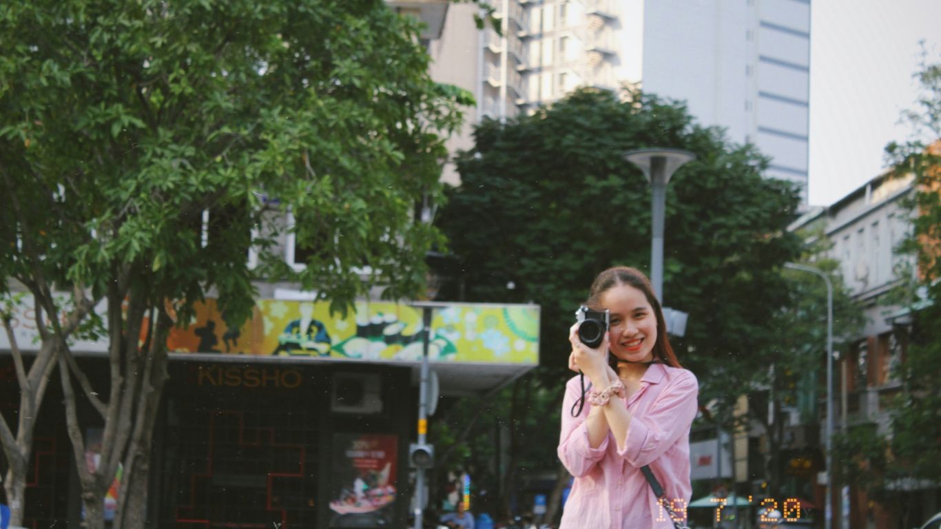 woman in pink coat holding black camera standing near green tree during daytime